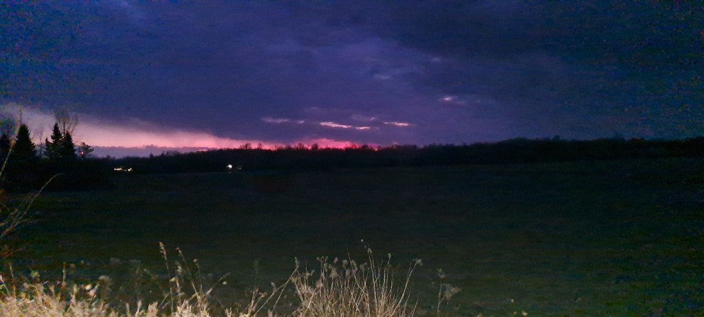 An empty field with a darkening sky with a magnificent thin stretch of pink clouds at the horizon.