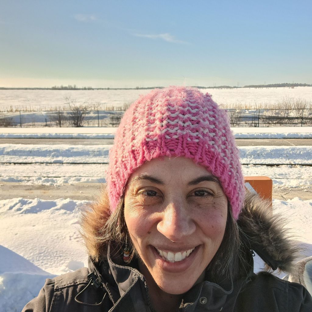 Photo of Bradlee smiling, wearing a pink winter hat in front of a snow covered field.