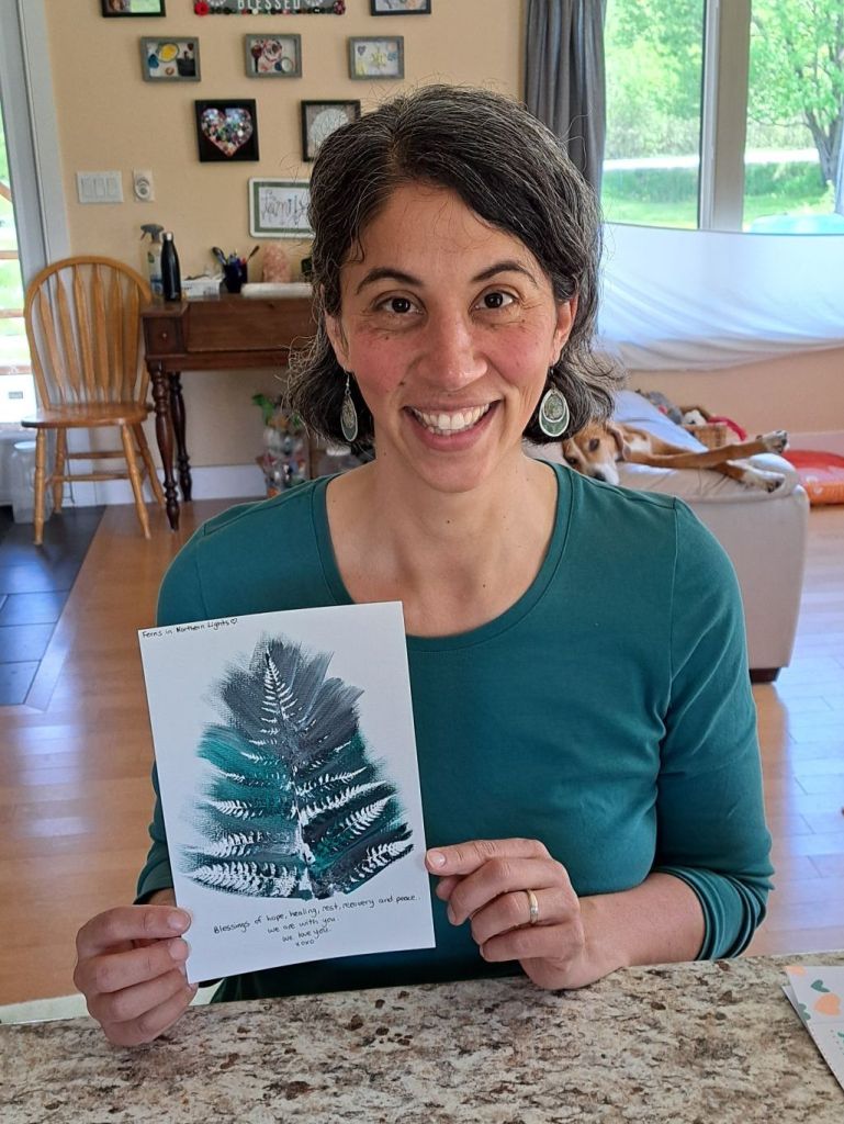 Bradlee holding up a white paper with art using paint colors and a fern from her woods.