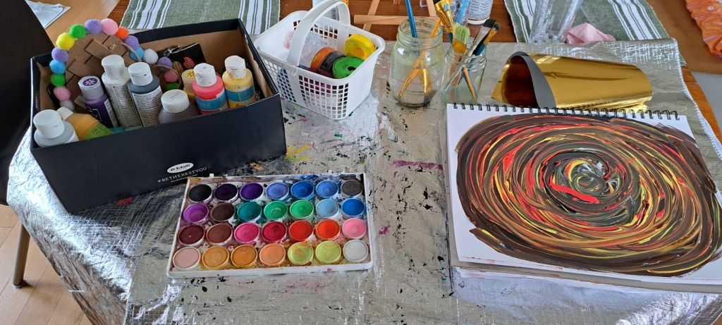 A silver tablecloth filled with all kinds of paints and brushes.