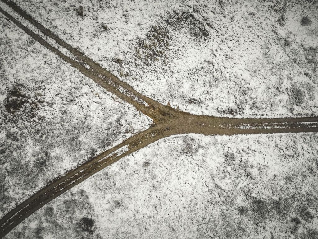 A dirt road through snowy terrain. It splits at one end and goes in two different directions.