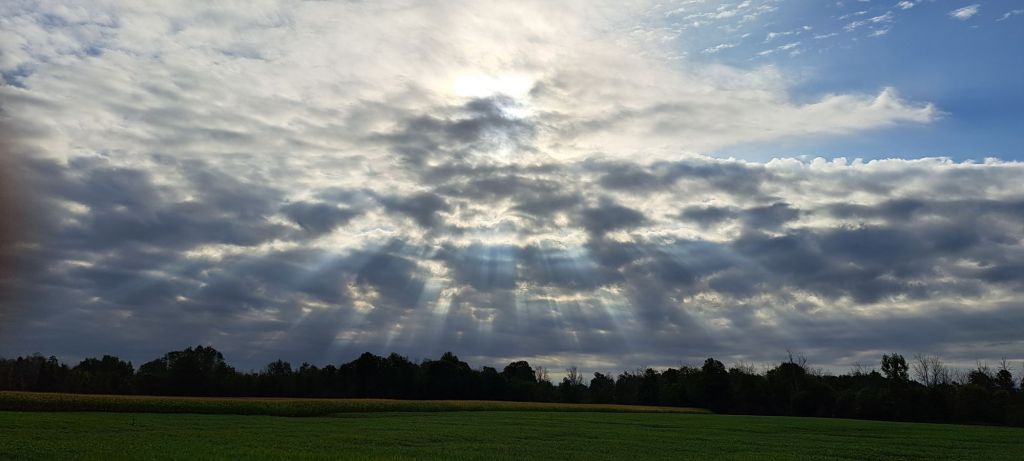A cloudy sky with rays of sunshine poking through the clouds in all directions, like it's trying to melt the clouds.
